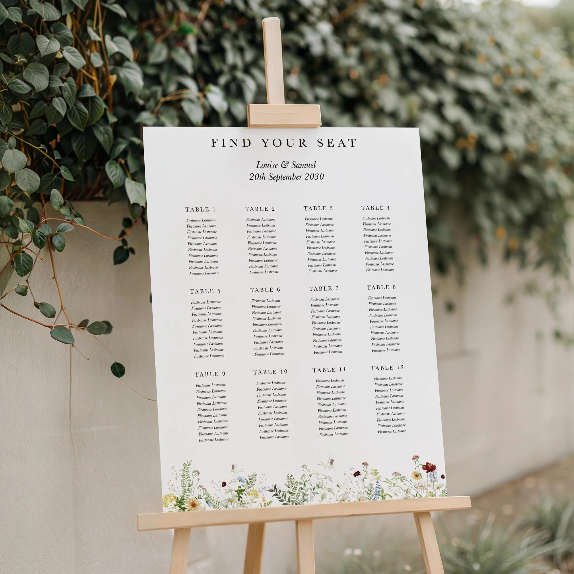 Meadow wedding seating plan displayed on a wooden easel, featuring rustic wildflowers with multiple guest tables