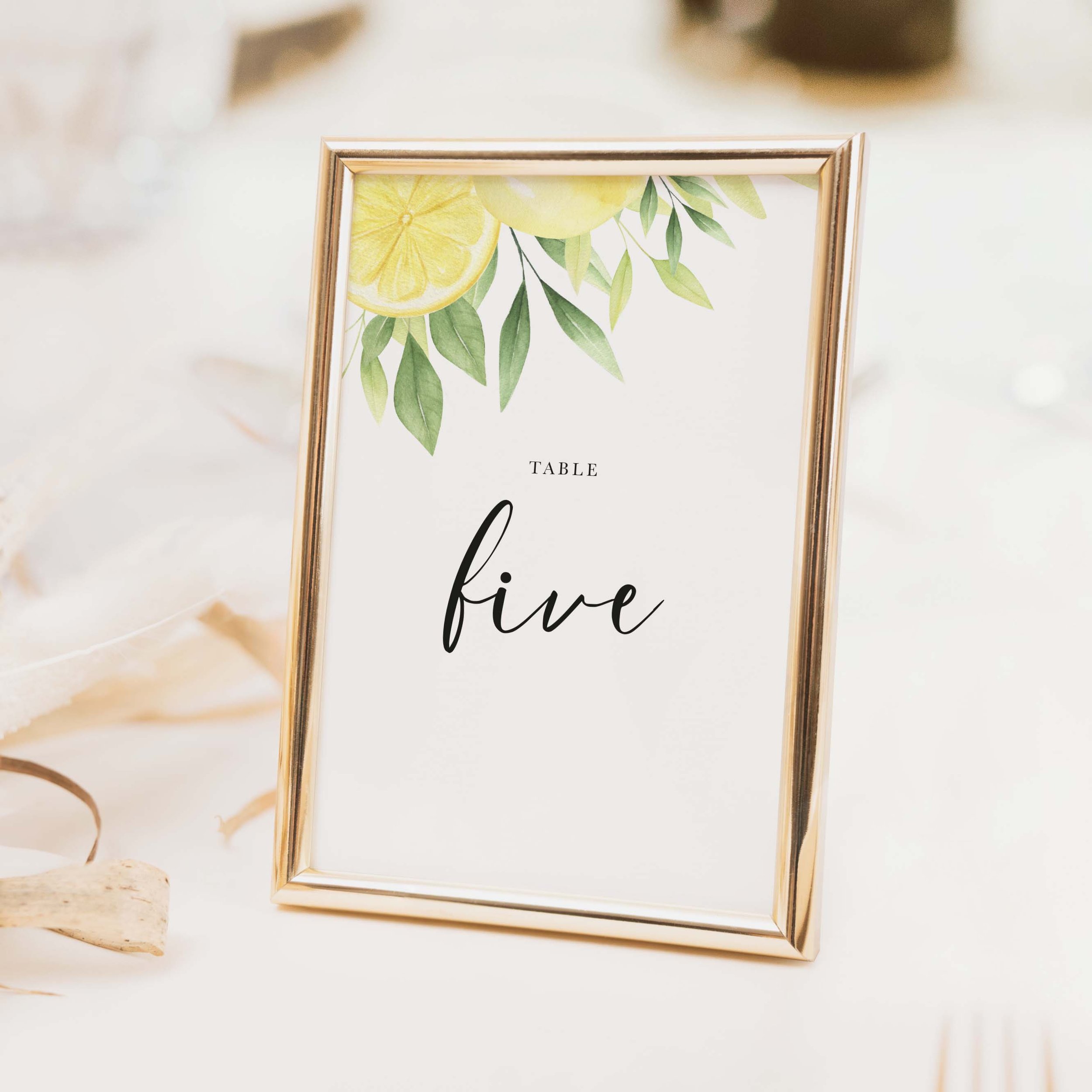 Lemon wedding table number with citrus botanical lemon and green foliage illustration and calligraphy script typography on luxury off-white card