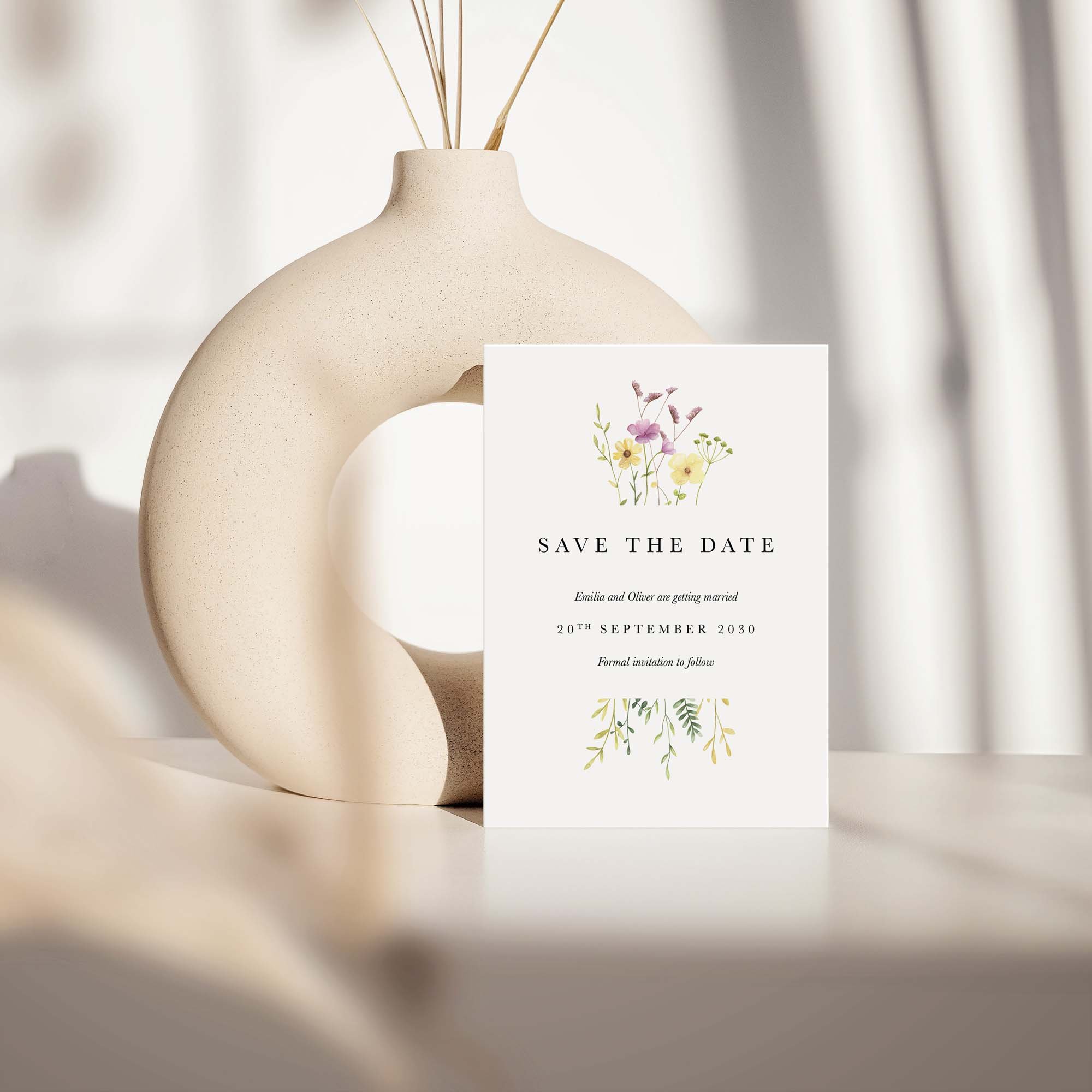Wildflower save the date card with colourful wildflowers design displayed against a cream ceramic vase on a neutral background