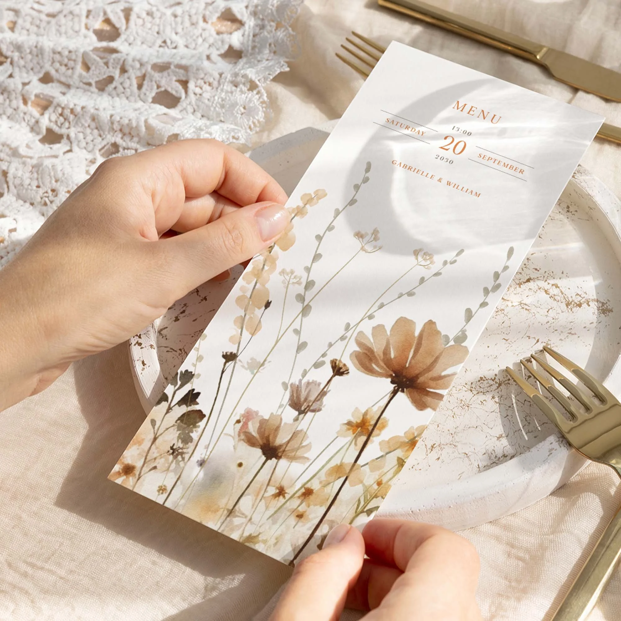 Hand holding a Field Harvest wedding breakfast menu card with a warm autumn wildflower meadow border illustration