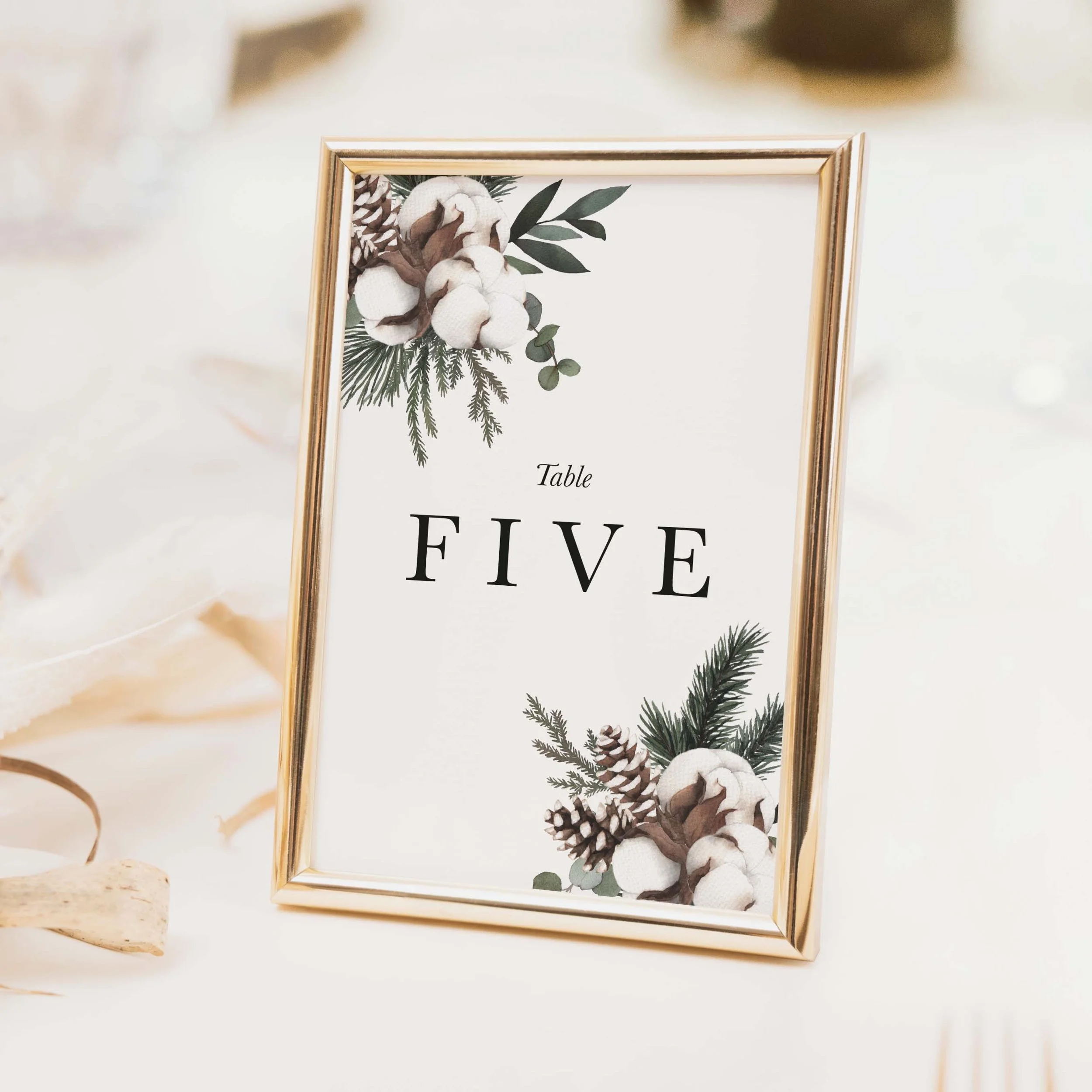 Woodland wedding table number with dark pine botanical pinecone and winter foliage illustration and clean modern typography on luxury off-white textured card