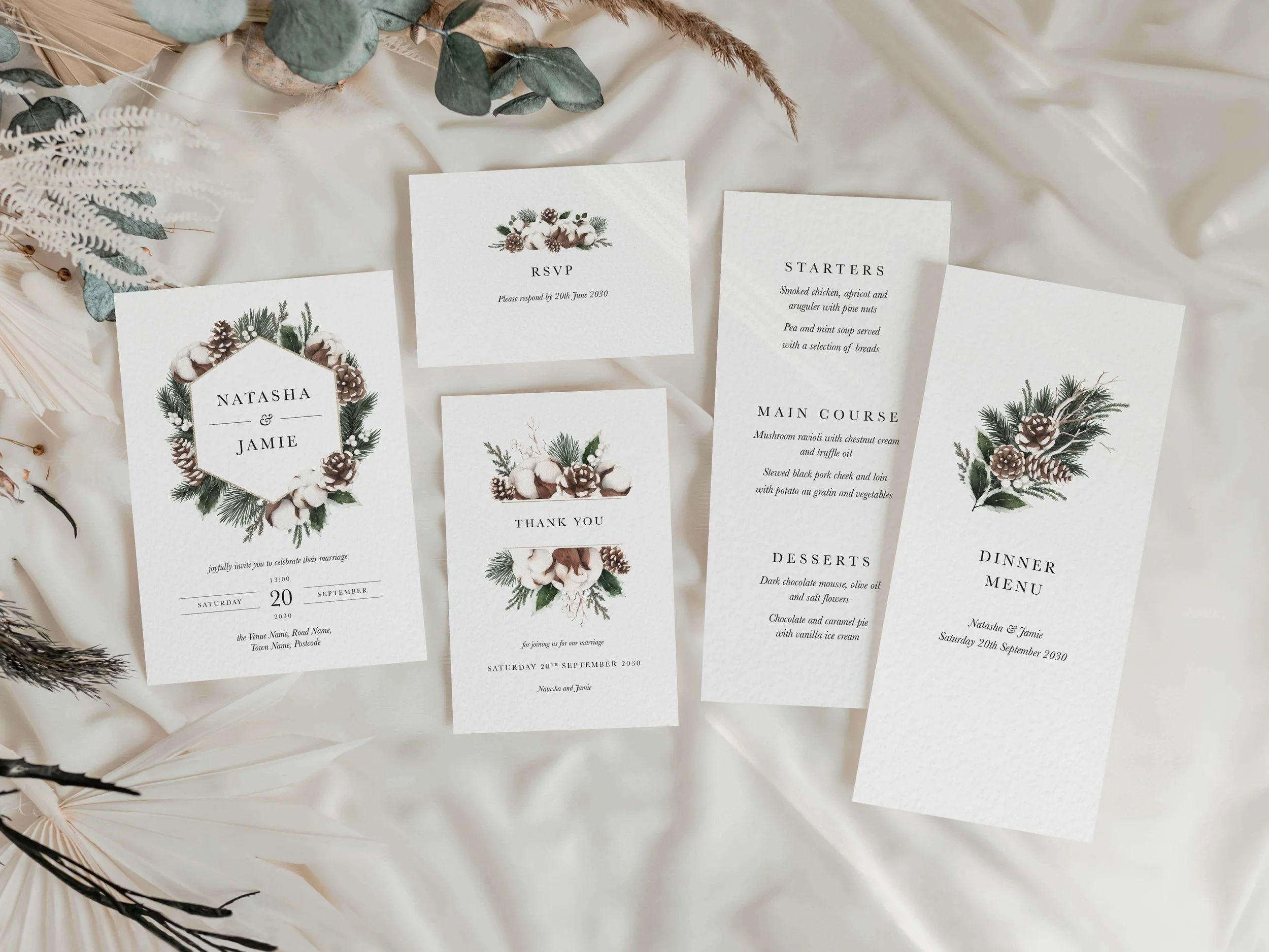 Full Woodland wedding stationery suite flat lay showing invitations, RSVP cards and coordinating pieces with pine cone, cotton and evergreen botanical design