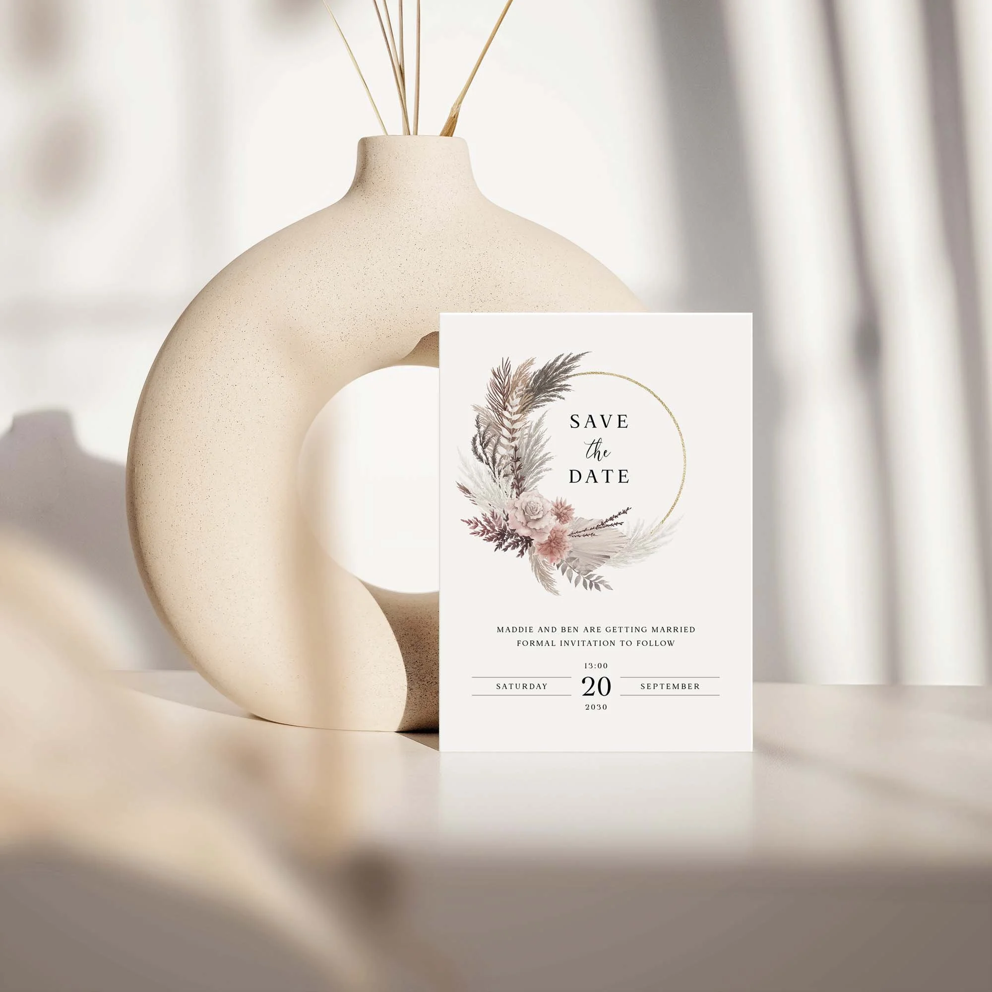 Blush Boho save the date card with pampas and blush floral design displayed against a cream ceramic vase on a neutral background
