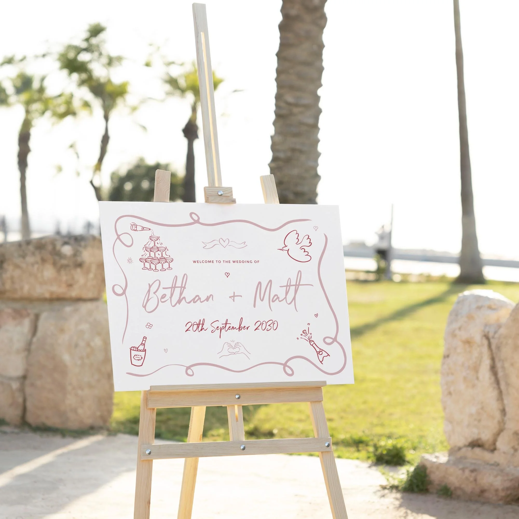 Pink Doodle wedding welcome sign displayed outdoors at a wedding venue on an easel