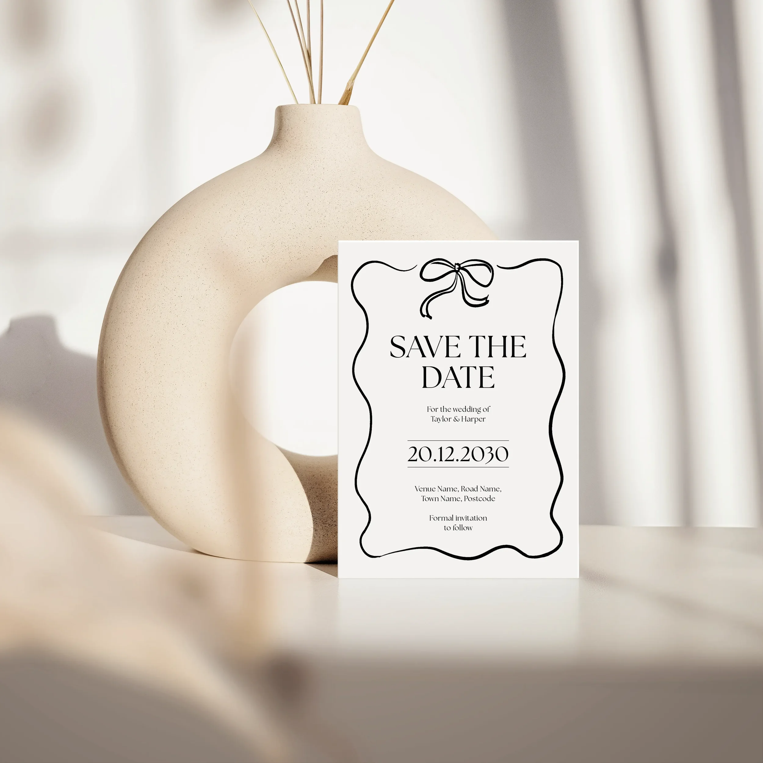 Black and white save the date card with bow illustration and wavy decorative border, styled against a ceramic vase — Black Tie wedding stationery collection