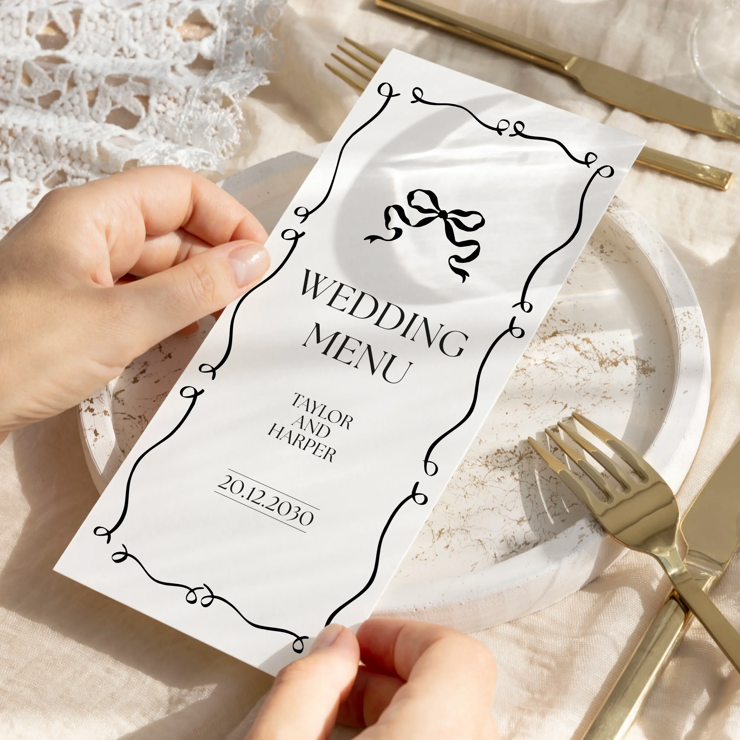 Hand holding a black and white wedding menu card with large bow illustration and decorative looped border — Black Tie collection by Wonder Wedding Stationery