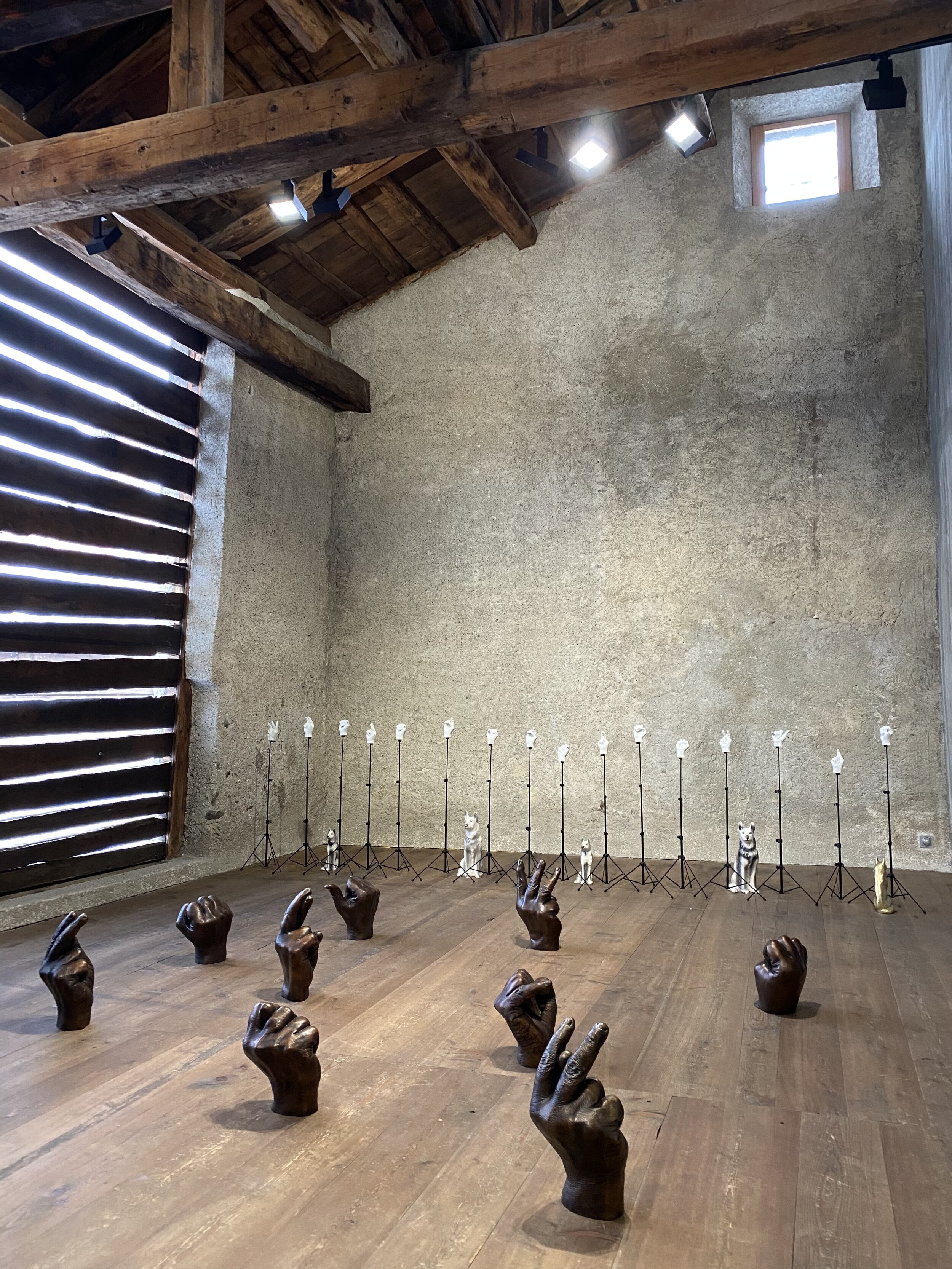 Galerie Tschudi, Zuoz (the typical Engadine Anti-White Cube Gallery): Kemang Wa lehulere, Where Did the Sky Go, 2020, 16 Bronze life size hands on 16 music stands- 16 bronze large hands - bronze dog head.