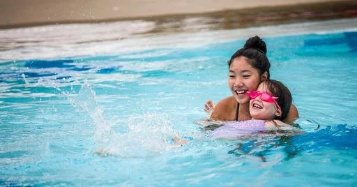 A woman and a young girl enjoying time together in a swimming pool, smiling and playing. Swimming Lessons