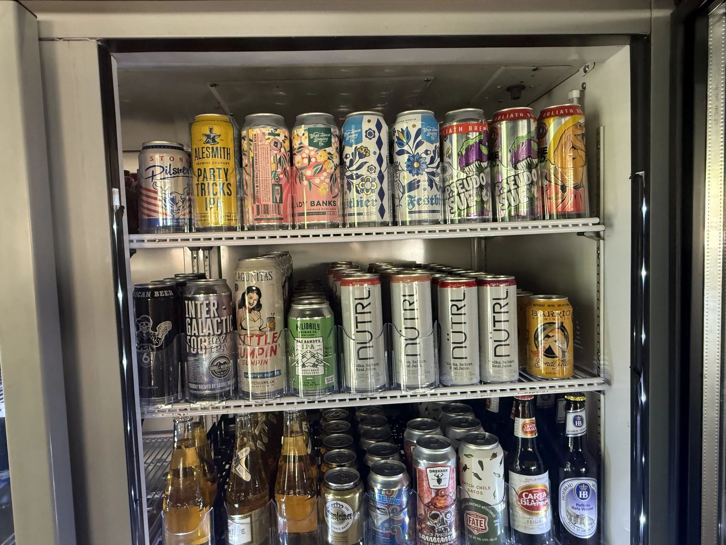 Park Centrals best bar 'The Green Woodpecker' Location of Arcadia Rotary clubs Annual Poker Tournament. A refrigerator with three shelves filled with various cans and bottles of beverages, including craft beers, sodas, and Spirts options for Drinks. 