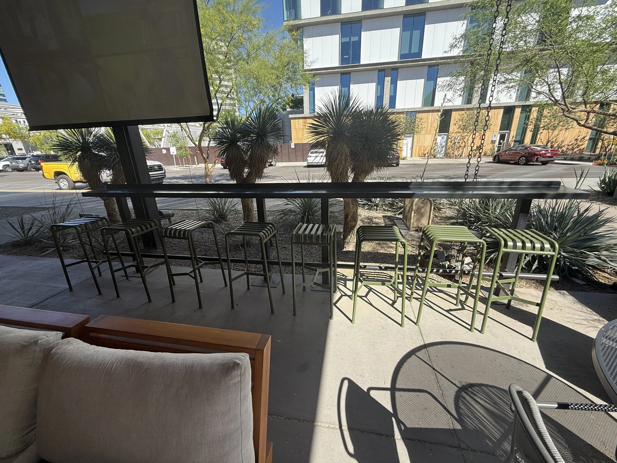 Cover patio view of a social area with beige couch, bar-height chairs, and a view outside through large windows at Park Central in Phoenix Arizona. Location for Phoenix Arcadia Rotary Club annual poker tournament at the green woodpecker