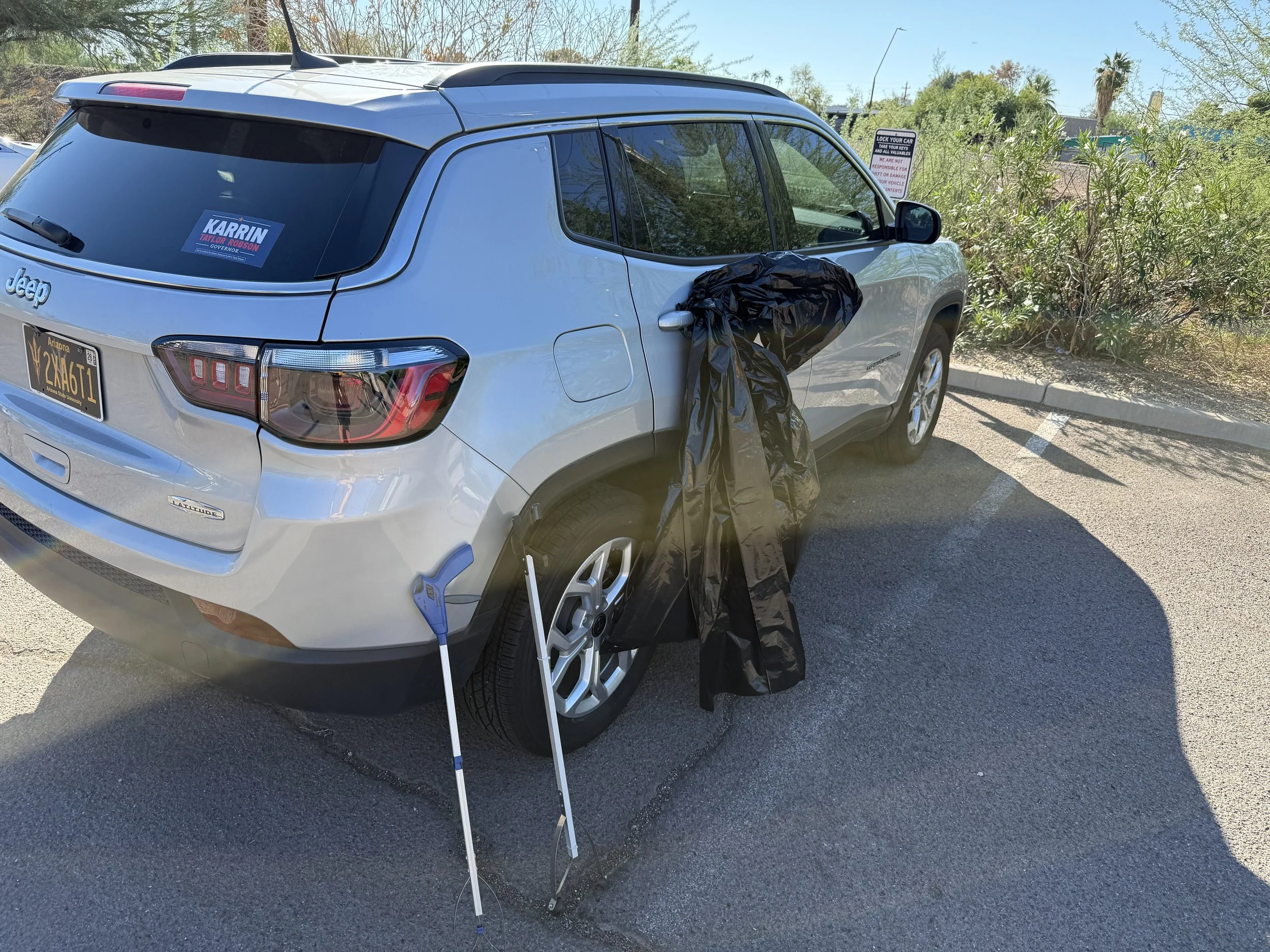 Silver Jeep SUV parked in a designated parking space with a black plastic bag hanging from the driver's side mirror.  Cale Prepping his car for Phoenix Arcadia Rotary Club volunteers cleaning streets along Indian School Road