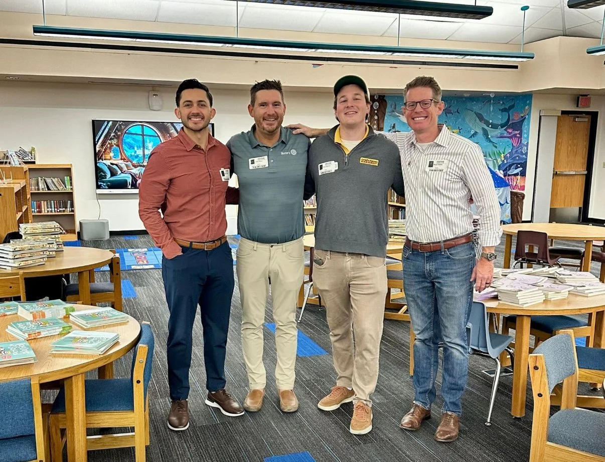 Four men standing in a library Phoenix Arcadia Rotary Club President Cale Ottens (2024-2025), Colin Deckwa, Bryce K, & Sharif Ahmed delivered books to a Title 1 school in Phoenix, Arizona, promoting literacy and educational opportunities. 
