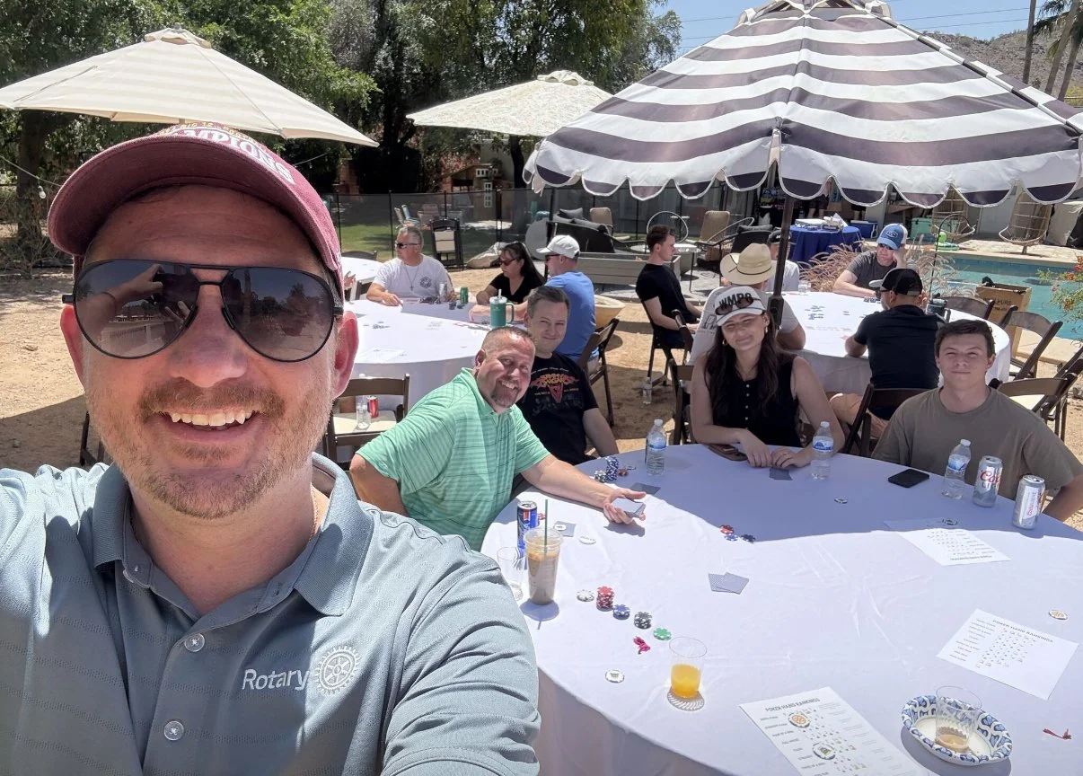 A man wearing sunglasses and a Rotary shirt taking a selfie at an outdoor event with several people at Phoenix Arcadia's First Ever Poker Tournament in May 2025