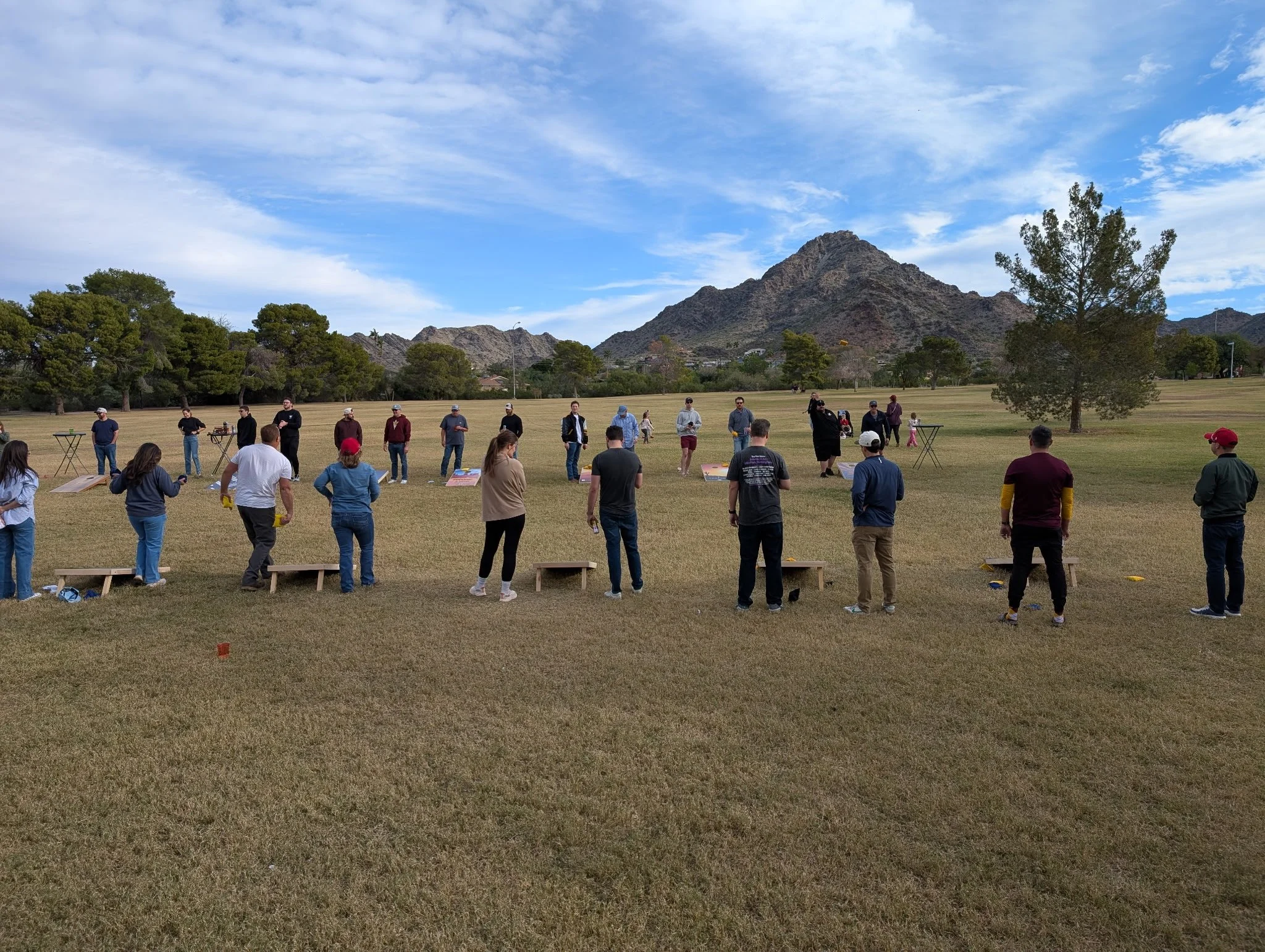 A group of people gathered outdoors in a large open field with mountains and trees in the background, participating in an organized activity.