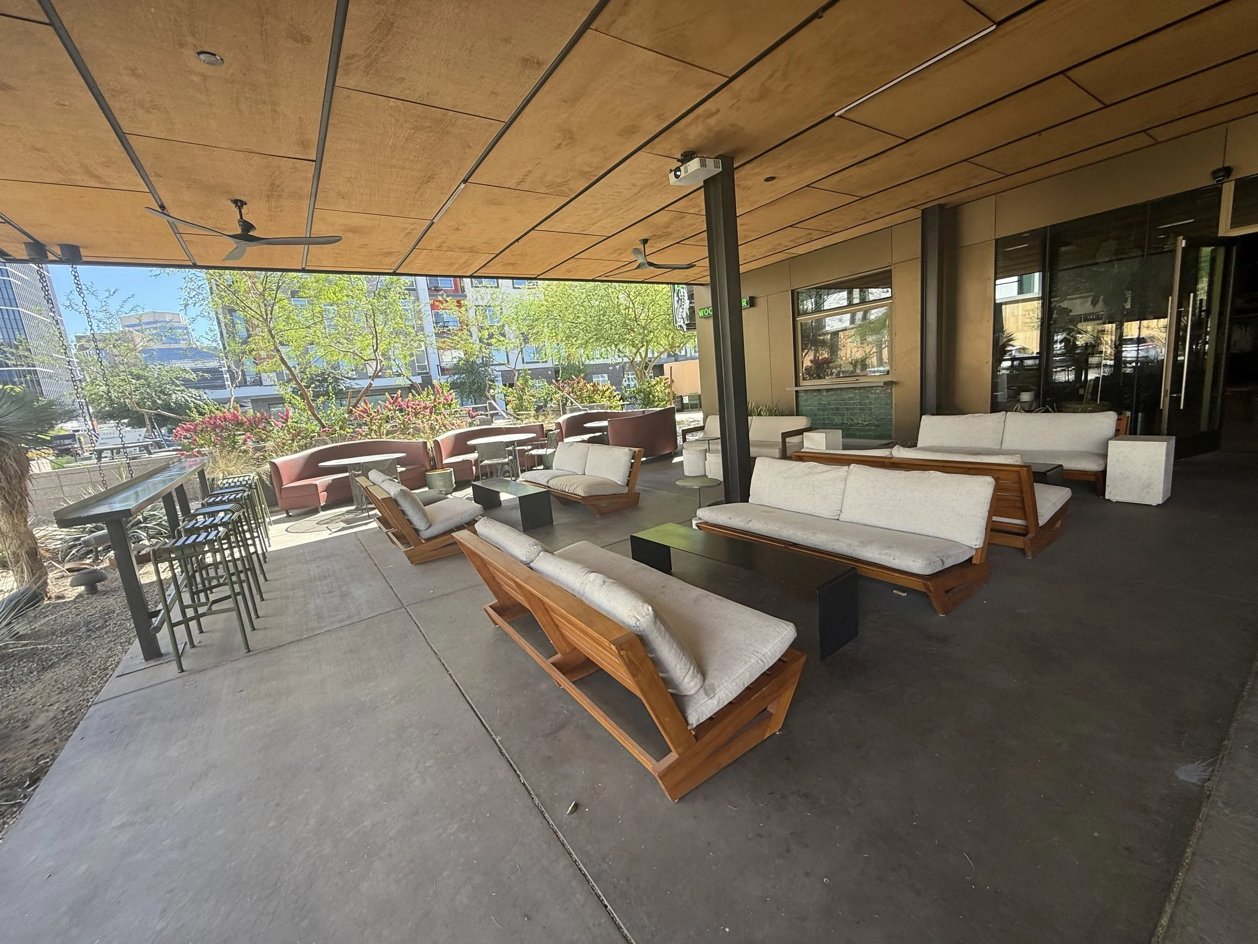 Outdoor seating area with modern lounge chairs, sofas, and high tables, greenery, and city buildings in the background. Park Centrals best bar 'The Green Woodpecker' Location of Arcadia Rotary clubs Annual Poker Tournament 