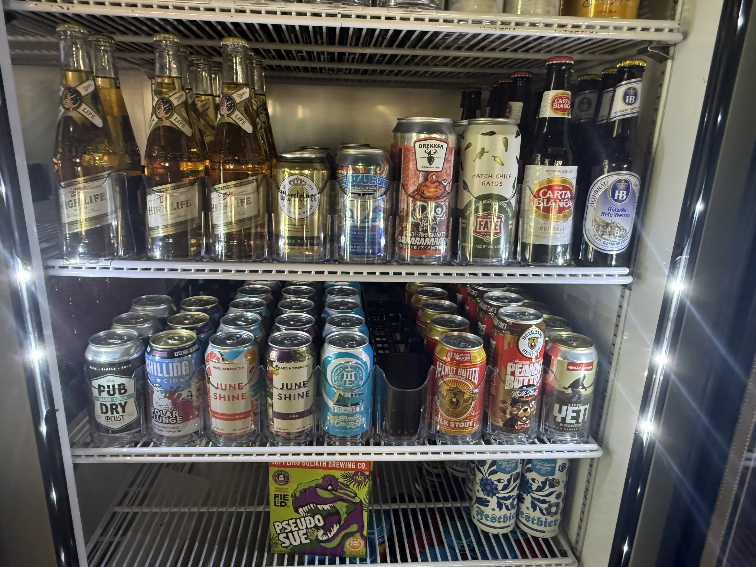 Park Centrals best bar 'The Green Woodpecker' Location of Arcadia Rotary clubs Annual Poker Tournament. A refrigerated display case filled with beer bottles and cans, with stacks of cans on the bottom shelf and bottles on the top shelf.
