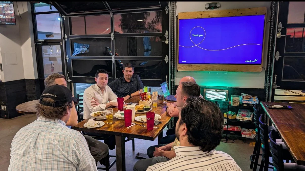 Members of the Phoenix Arcadia Rotary Club participate in a monthly speaker discussion at Tombstone Brewing Company in Phoenix, Arizona, with a presentation displayed on screen and sunset views in the background.