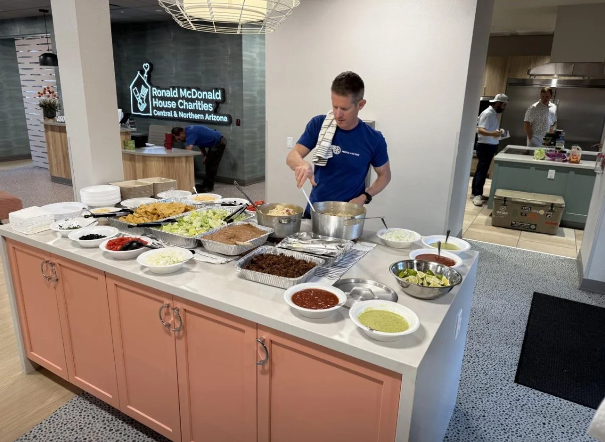 A man serving himself food at a buffet table with various dishes, including rice, salsa, lettuce, black olives, and lime wedges, at a Ronald McDonald House Charities event.