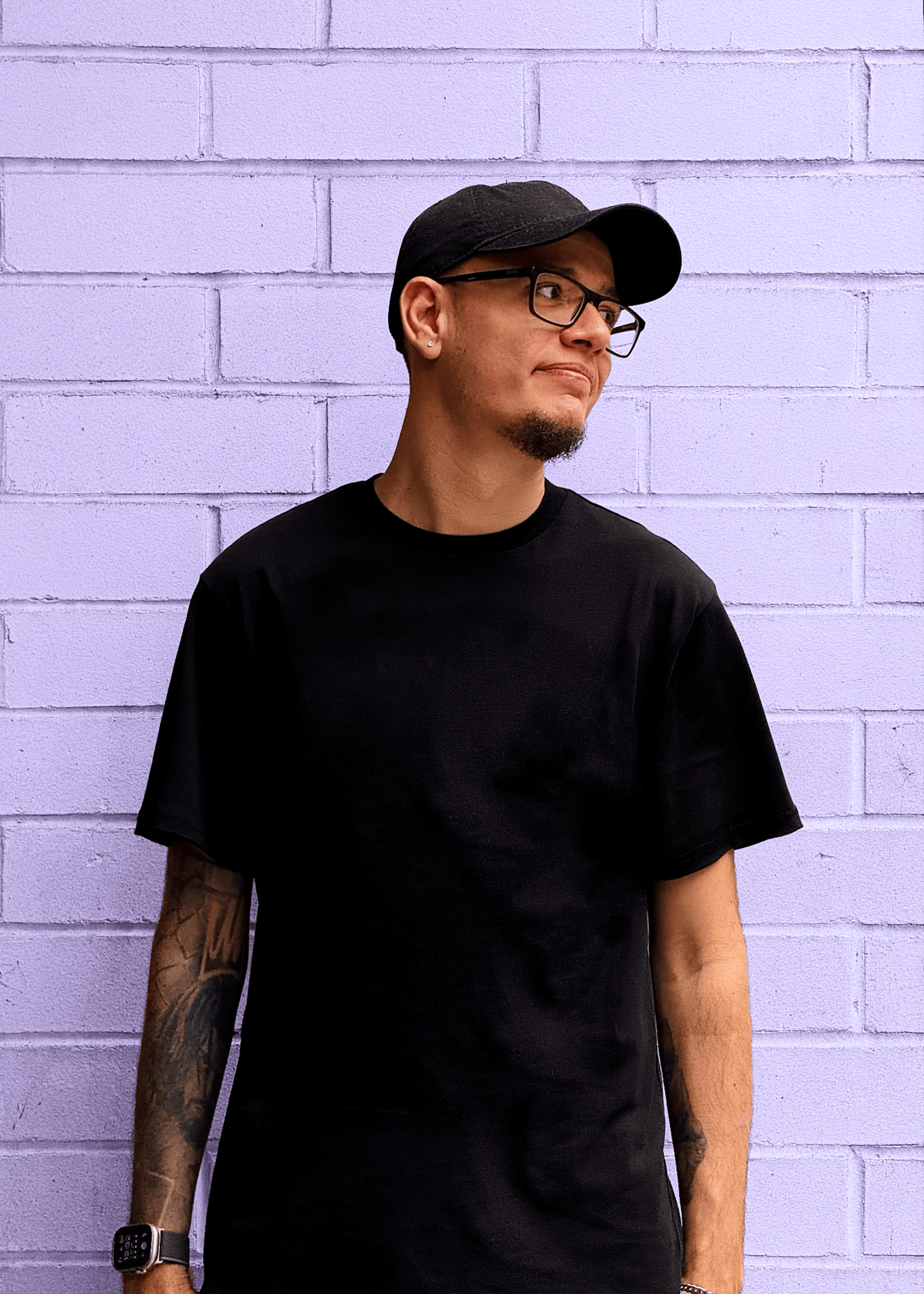 Image of me against a brick wall, dressed in black, softly smiling and looking to the right side.