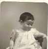 Young girl in a dress, sitting and looking down, black and white photo.