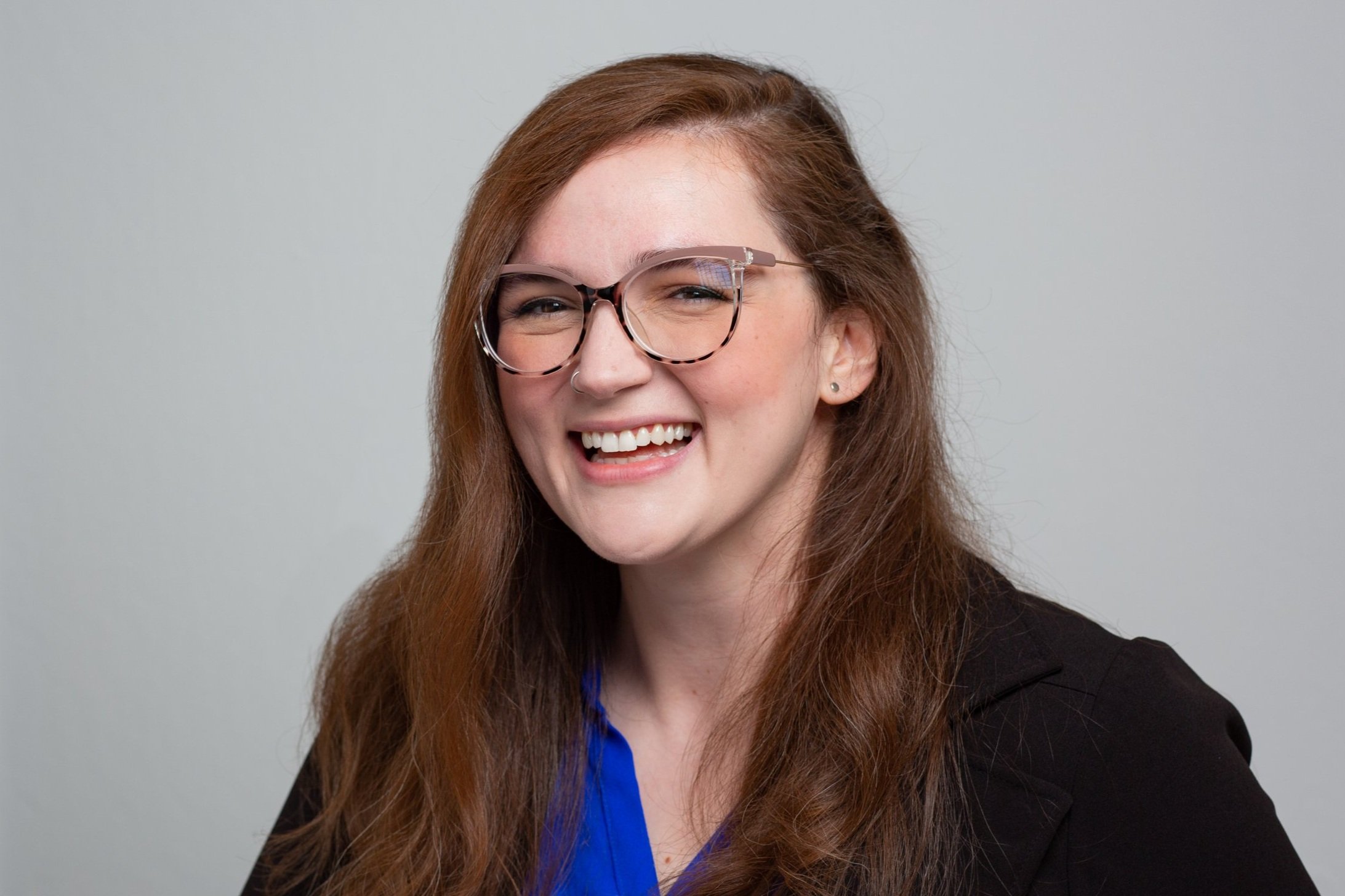 Lexie is smiling at the camera. She has glasses and long auburn hair.