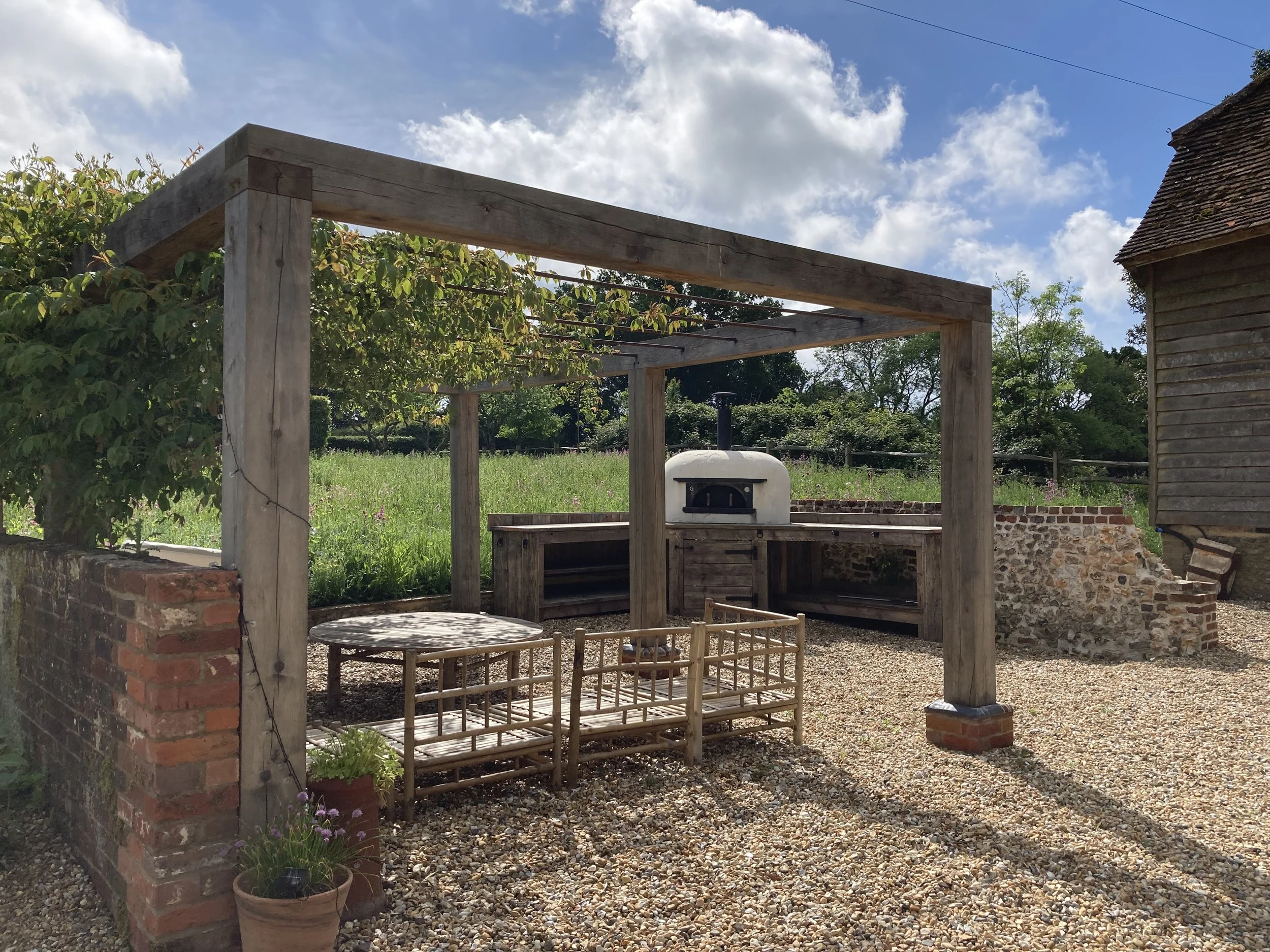 An oak and steel pergola provides support for a mature climbing rose and dappled shade for dining. 