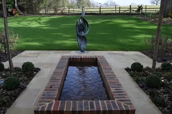 The water feature ripples gently from two submerged copper pipes. The herringbone brick at the bottom echoes the pattern of the interior floors.  