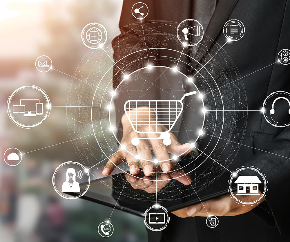 Person holding a tablet with a digital shopping cart icon and various technology and shopping-related icons around it, representing online shopping and digital commerce.