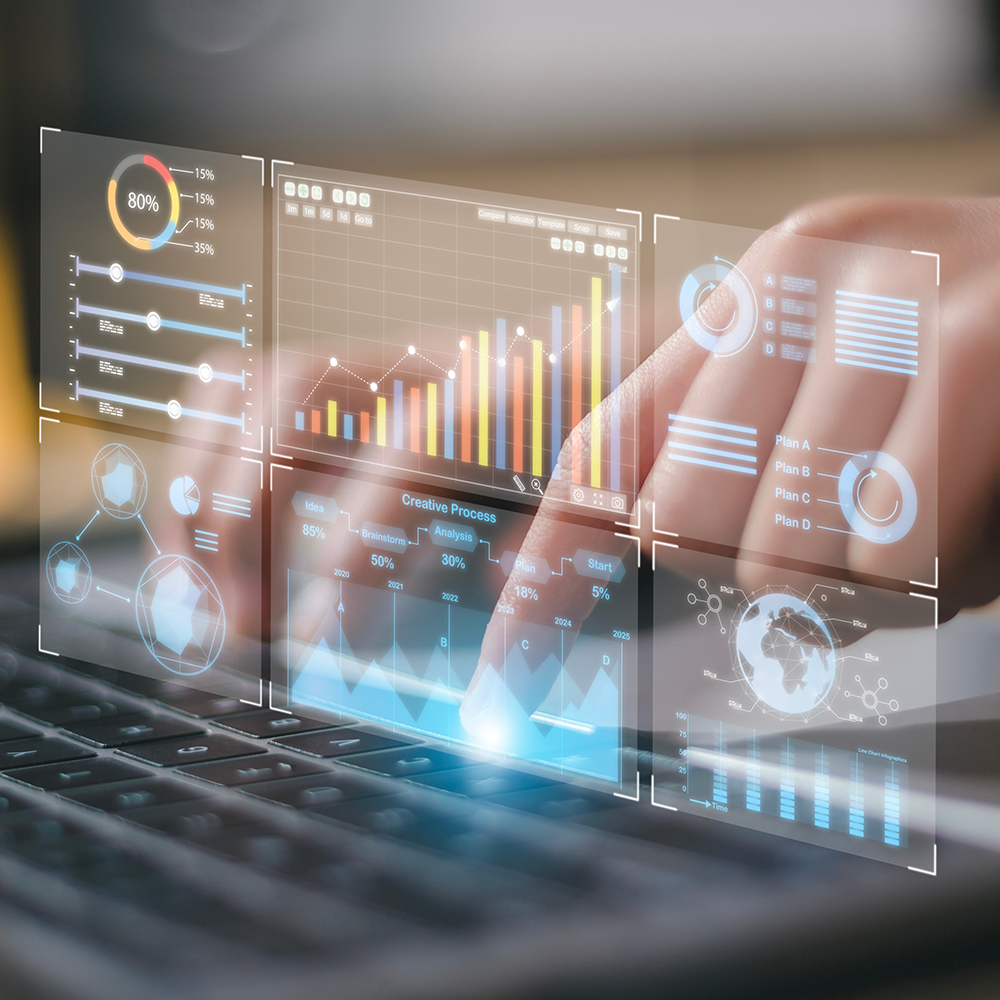 A person's finger interacting with a futuristic transparent digital dashboard displaying various charts, graphs, and analytics over a laptop keyboard.
