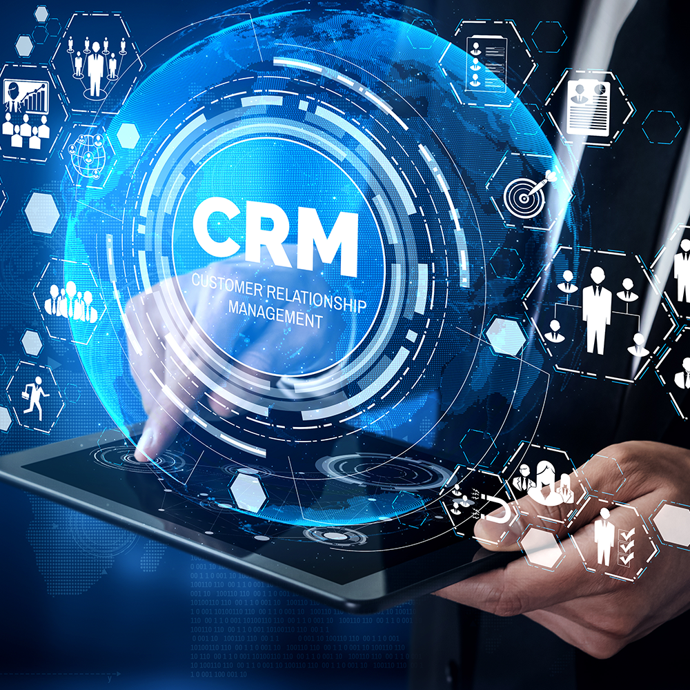 A person holding a tablet with a holographic display showing the words 'CRM Customer Relationship Management' surrounded by icons representing people, data, and communication, in a digital and technological style.
