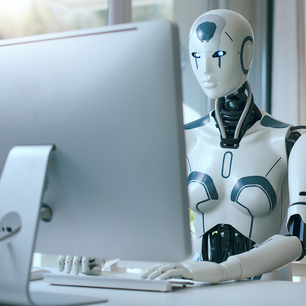 A humanoid robot with a white and black exterior working on a computer in a modern office setting.