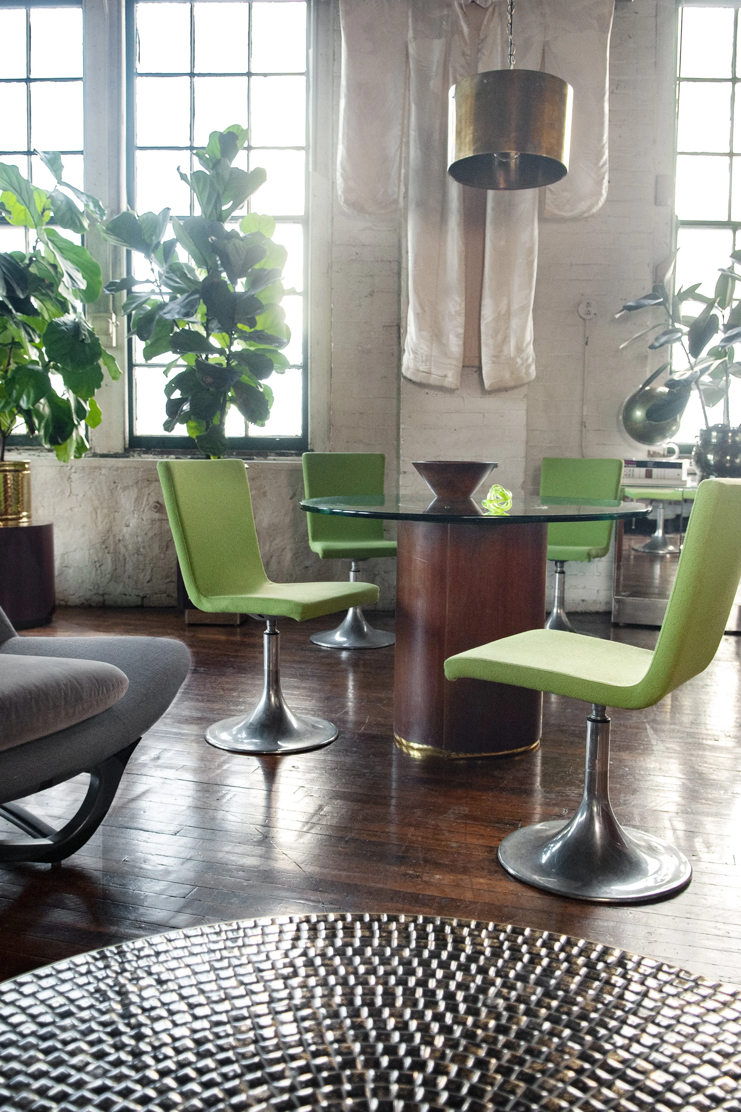 House of No Era's former historic loft studio in Camp Washington, Cincinnati, featuring a Paul Mayen-style cylindrical dining table styled with a set of 1970s Calligaris Italian lime-green dining chairs, a cylindrical brass pendant light, a 1970s mos