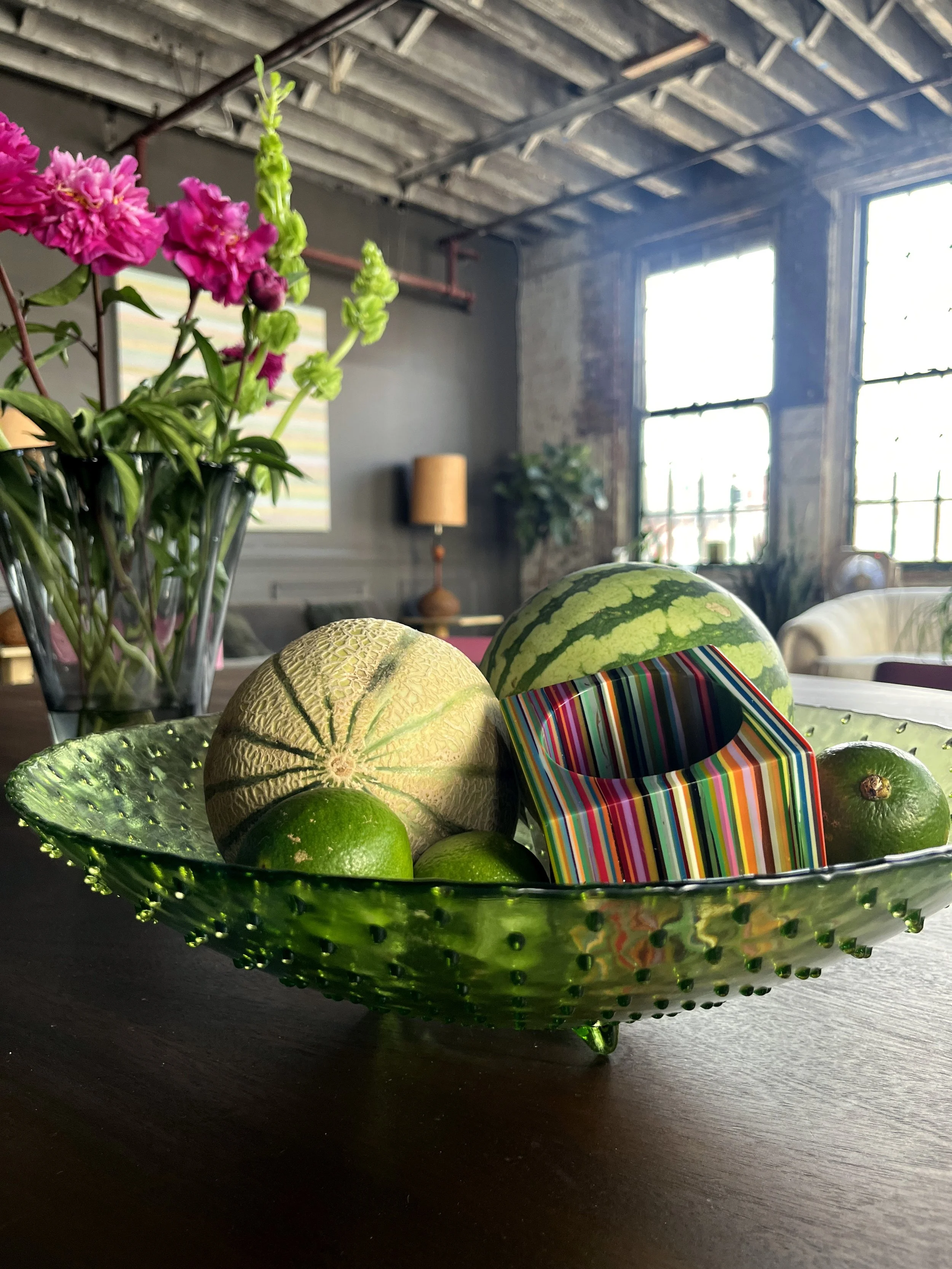 House of No Era's former historic loft studio in Camp Washington, Cincinnati, featuring a large green hobnail glass centerpiece bowl filled with an assortment of tropical fruits and tropical-inspired jewelry.
