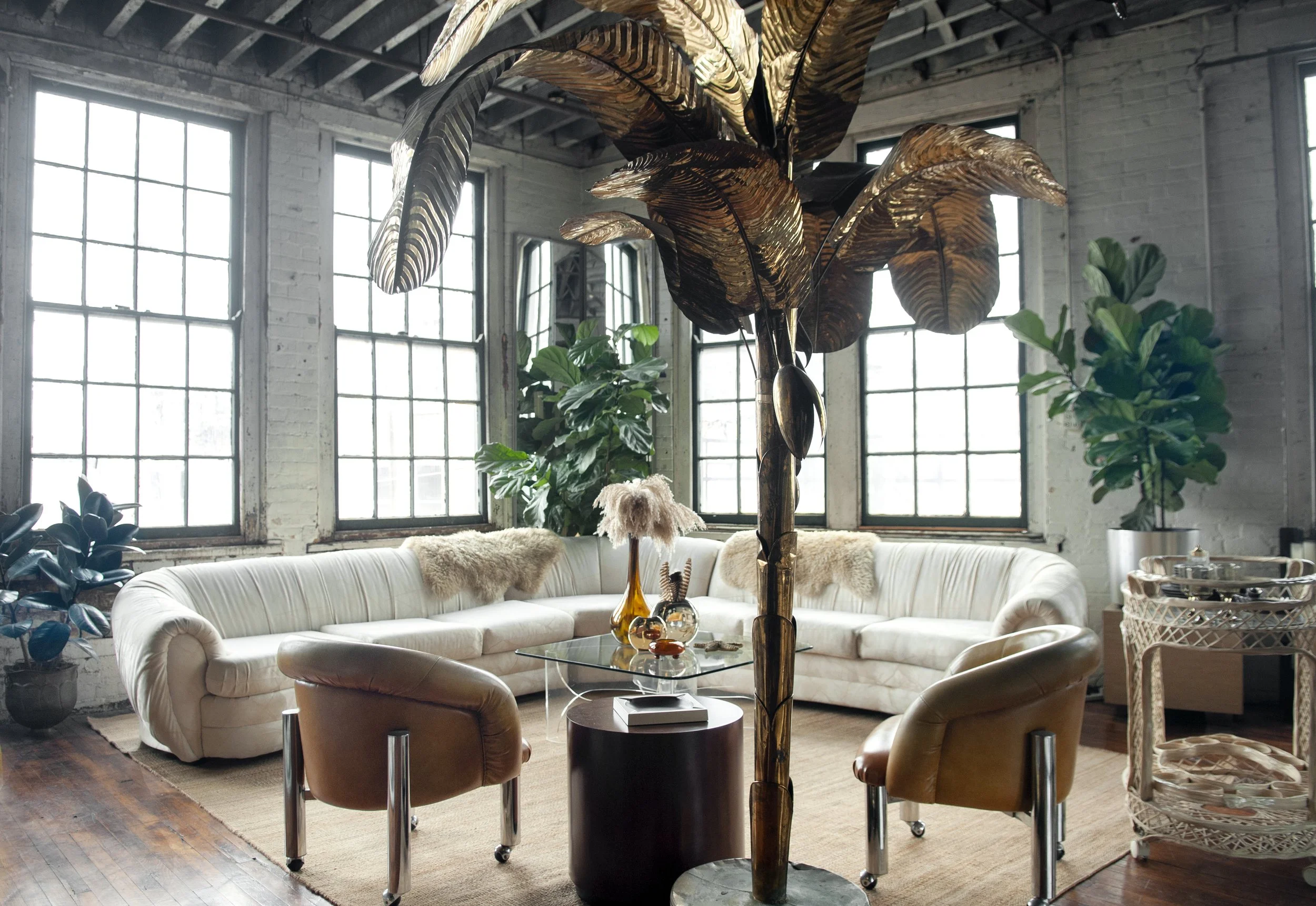 House of No Era's former historic loft studio in Camp Washington, Cincinnati, featuring an oversized white Vladimir Kagan sectional sofa, a Postmodern butterfly Lucite coffee table styled with vintage glassware and vases, a sculptural fiberglass bar 