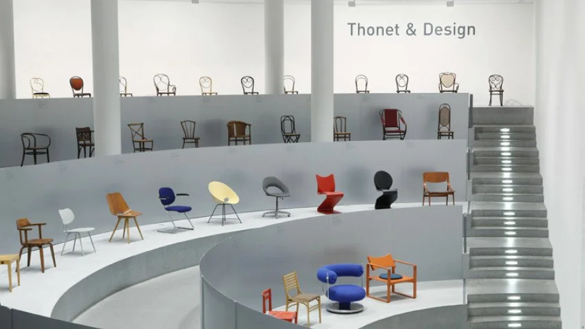 Rows of iconic Thonet chair designs arranged around a minimalist circular display beneath the Thonet logo, showcasing the evolution of furniture design across different eras.