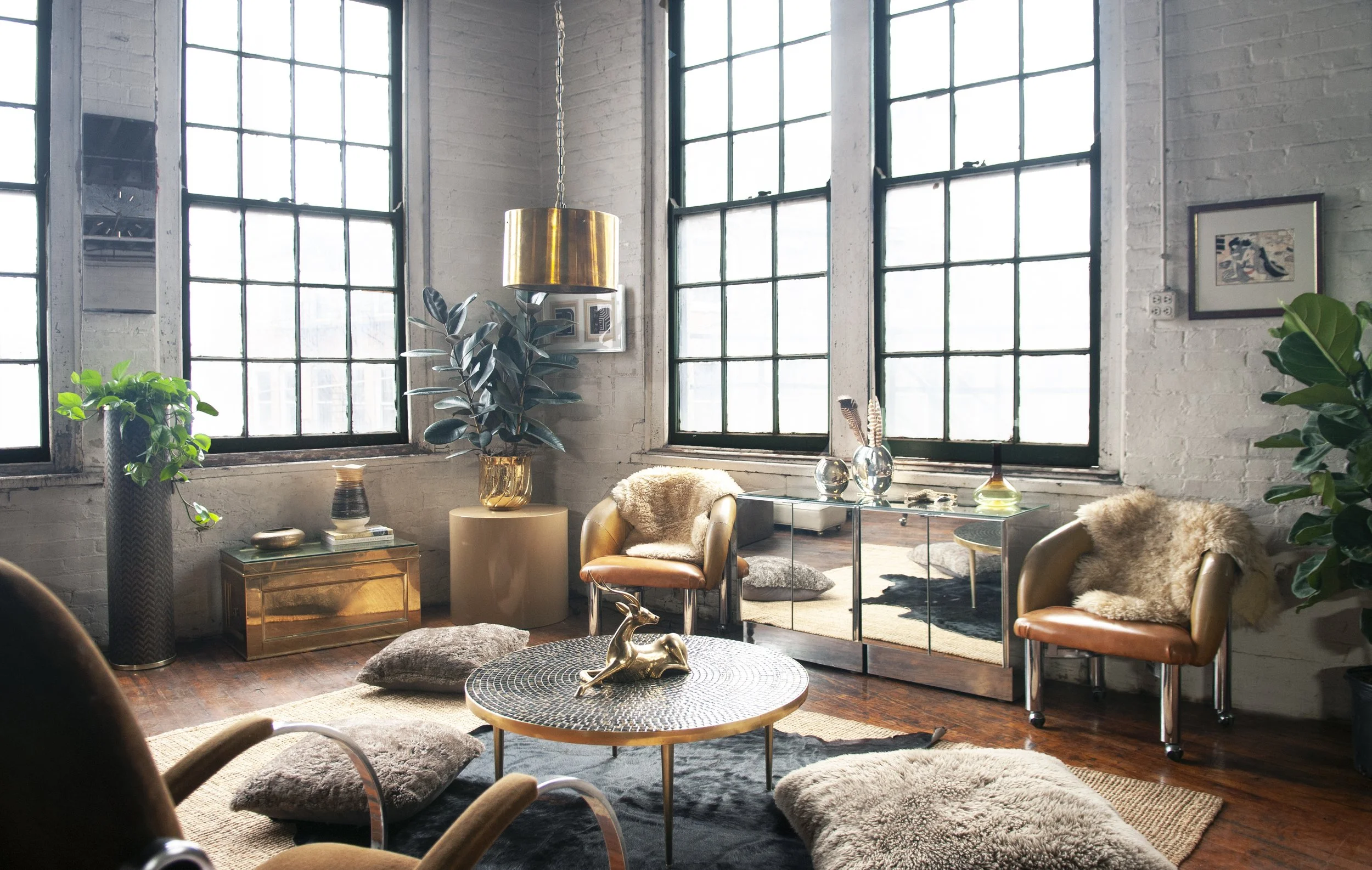 House of No Era's former historic loft studio in Camp Washington, Cincinnati, featuring a 1970s Italian mosaic-tiled coffee table, Milo Baughman lounge chairs on casters, a pair of Ello mirrored side tables, a 1970s brass campaign trunk, a large bras