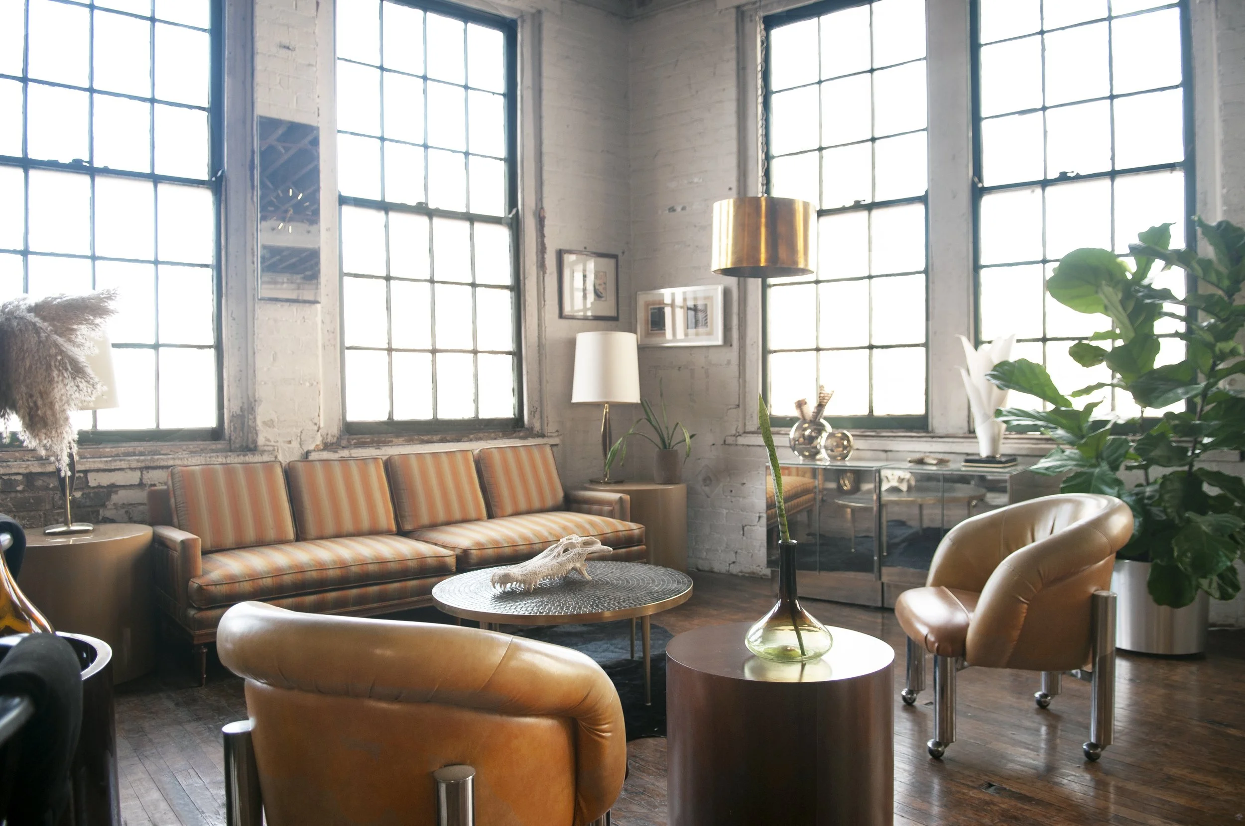 House of No Era's former historic loft studio in Camp Washington, Cincinnati, featuring a 1970s Hollywood Regency yellow-and-copper-striped silk sofa, a pair of Ello mirrored bedside tables, a 1970s Italian mosaic-tiled coffee table, Milo Baughman lo
