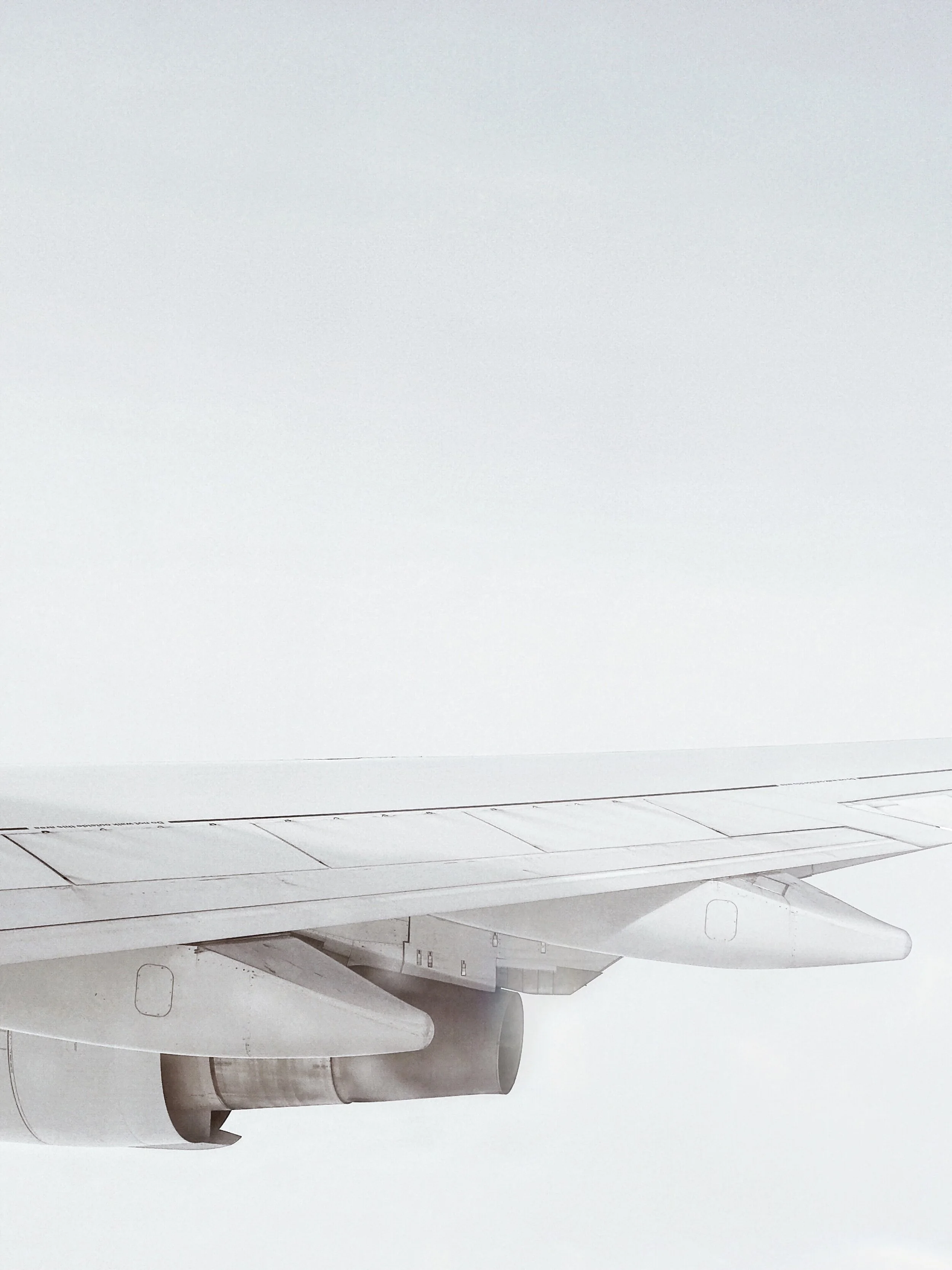Side view of an airplane wing and engine flying through cloudy sky.