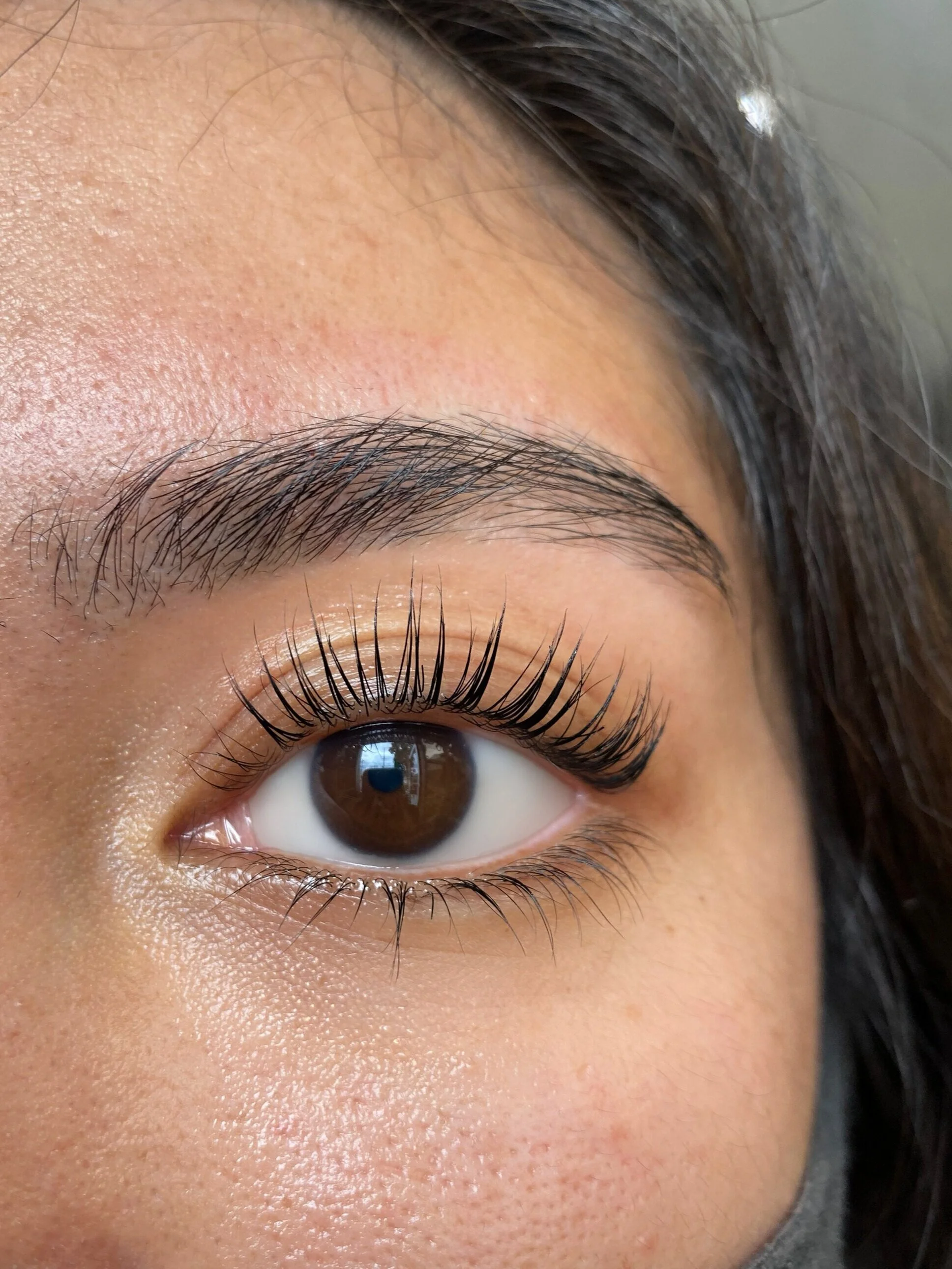Close-up of a woman's eye with long, curled eyelashes, arched eyebrow, and smooth skin.