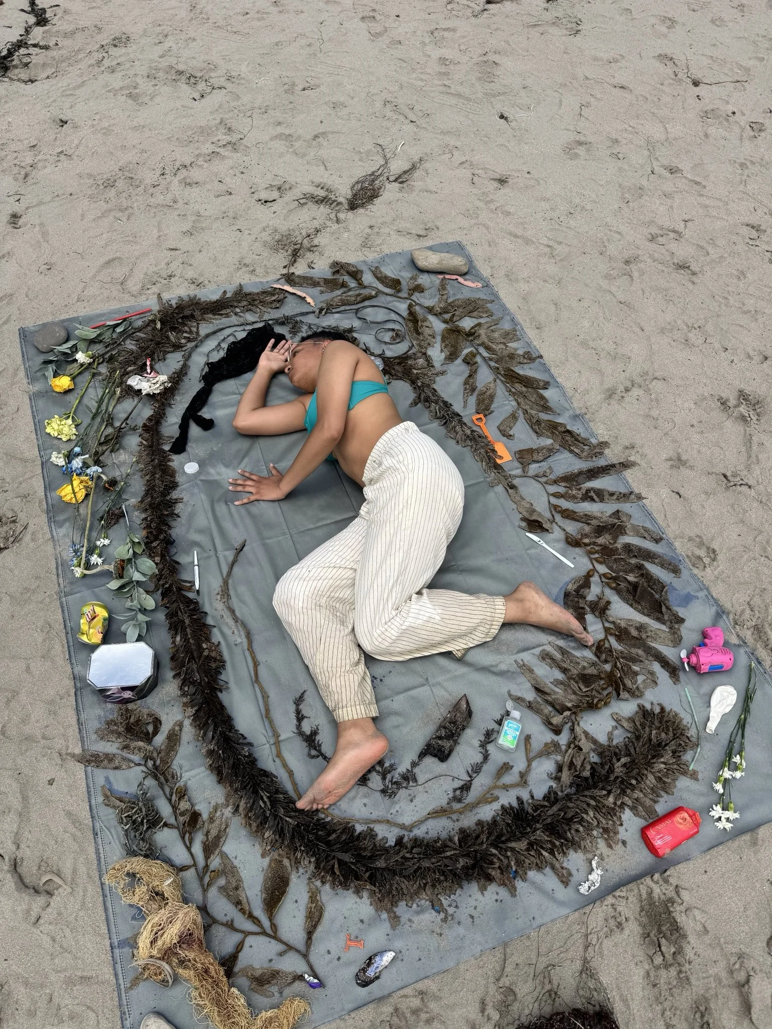 Schessa Garbutt lays on cyanotype fabric with kelp and beach trash to create “Plastocene (eco-spiritual no. 2)” Photo by William Rouse.  (2025)