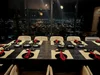 Elegant dining table with black plates and red napkins set for a meal, with a cityscape view through large windows at night.