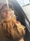 Woman smiling with a large, fluffy dog in a car by an open window.