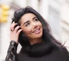 Smiling woman outdoors, touching her hair, wearing a black outfit.