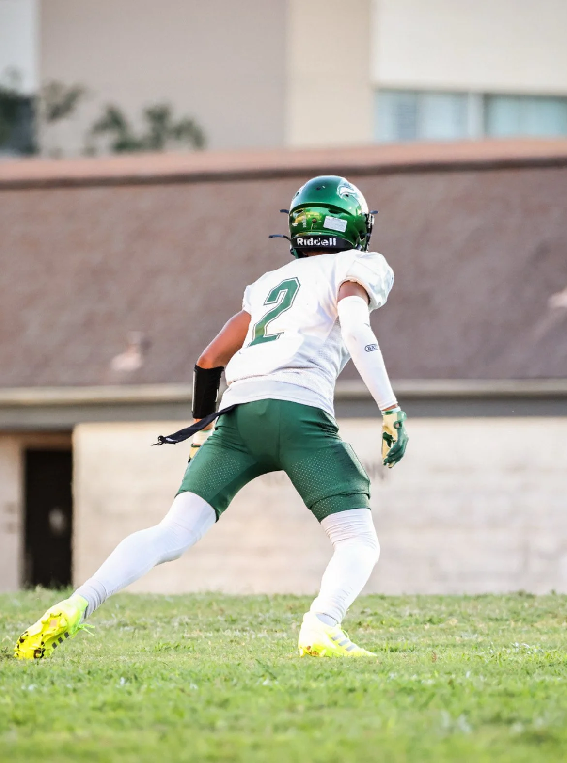 An American football player in a white and green uniform, wearing a green helmet with a logo, on a grassy field.
