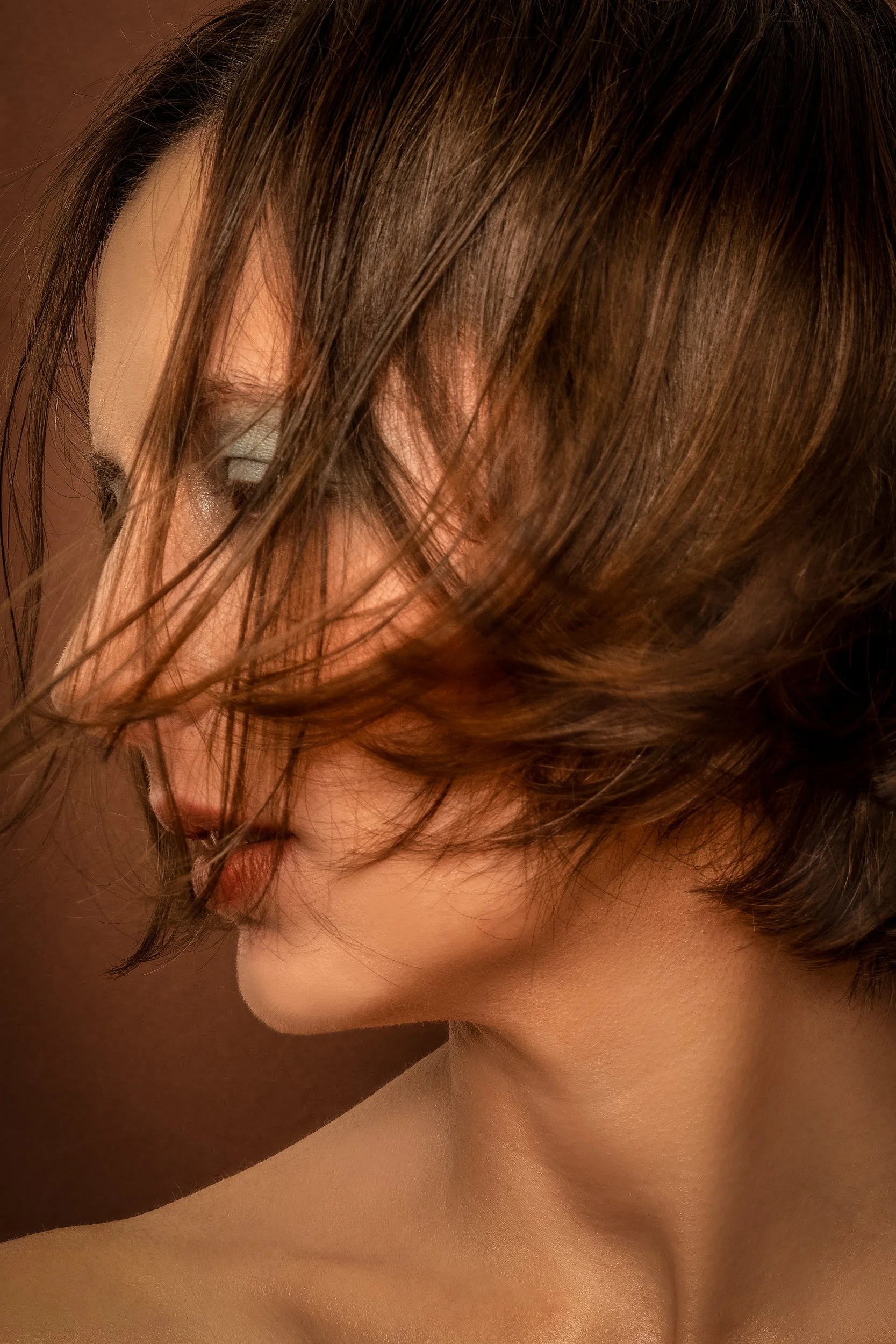 Close-up of a woman's face with her hair partially covering her face, showing her eye, nose, and neck.