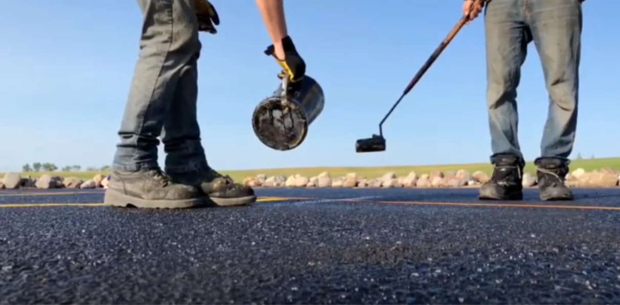 Two workers applying tar to asphalt pavement