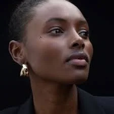 Close-up of an African American woman with natural hair and gold hoop earrings, looking to the side against a dark background.