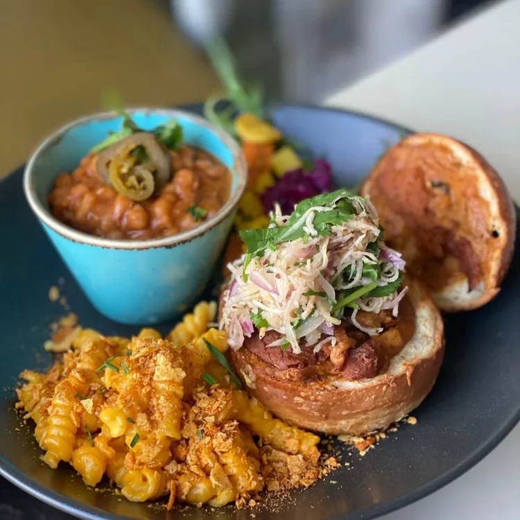 Plate of food including baked stuffed roll topped with coleslaw, macaroni and cheese, baked beans, and cornbread.