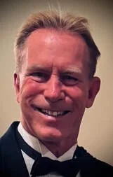 A smiling man in formal attire, wearing a tuxedo and bowtie.
