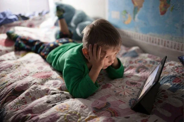 A child relaxing on a bed while watching a movie.